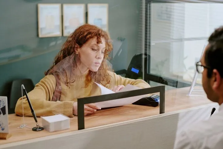 Front-desk clerk checking a document with a customer waiting on the other side